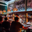 Interiors of Alma Luna, a busy bar with tropical paintings overhead.