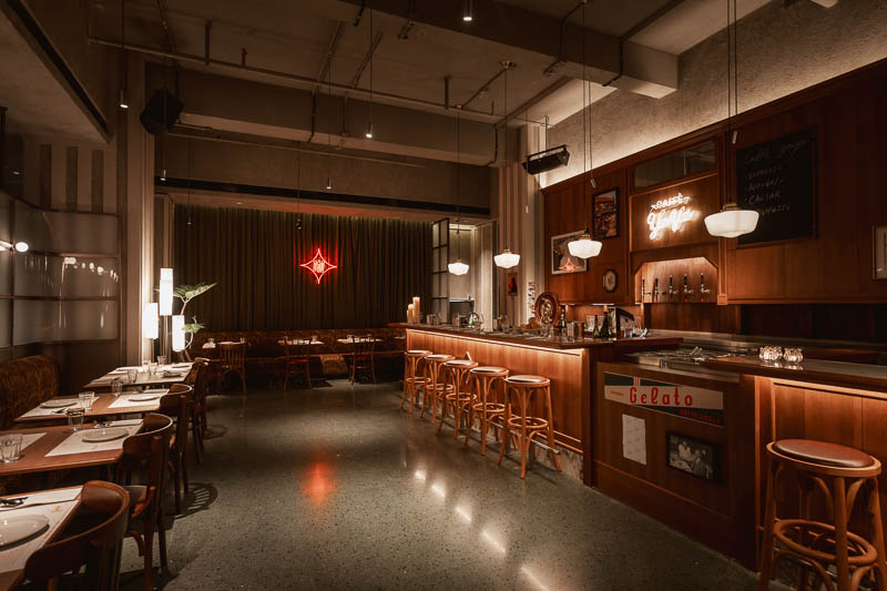 Interiors of Caffe Yaya restaurant show warm wood accents, casual seating and a handsome bar with gelato sign.